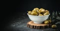 Close up shot of green olives in a white bowl on the wooden stand with olive leaves on a black background. Traditional Greek and Royalty Free Stock Photo