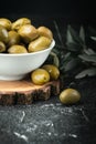 Close up shot of green olives in a white bowl on the wooden stand with olive leaves on a black background. Traditional Greek and Royalty Free Stock Photo