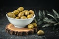 Close up shot of green olives in a white bowl on the wooden stand with olive leaves on a black background. Traditional Greek and Royalty Free Stock Photo