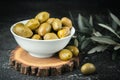 Close up shot of green olives in a white bowl on the wooden stand with olive leaves on a black background. Traditional Greek and Royalty Free Stock Photo