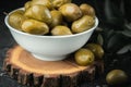 Close up shot of green olives in a white bowl on the wooden stand with olive leaves on a black background. Traditional Greek and Royalty Free Stock Photo