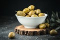 Close up shot of green olives in a white bowl on the wooden stand with olive leaves on a black background. Traditional Greek and Royalty Free Stock Photo