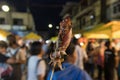 Close-up shot of a grilled squid on a stick in the background of the blurry crowd on a market