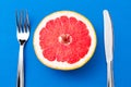 Half of ripe grapefruit, knife and fork on colored background Royalty Free Stock Photo