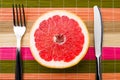 Half of ripe grapefruit, knife and fork on colored background Royalty Free Stock Photo