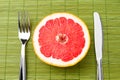 Half of ripe grapefruit, knife and fork on colored background Royalty Free Stock Photo