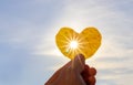 Close up shot of hand holding yellow leaf of heart shape with sun rays shining through it