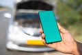 Close up shot of hands showing green screen mobile phone in front of broken car on highway - concept of online booking Royalty Free Stock Photo