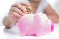 Close up shot hands of woman putting gold bitcoin to pink piggy