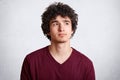 Close up shot of handsome curly teenager man looks pensively upwards, being deep in thoughts, ponders about future plans, isolated Royalty Free Stock Photo