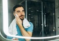 Close-up shot of handsome young man with towel in his neck standing in front of mirror and applying shaving foam to his Royalty Free Stock Photo