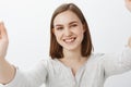 Close-up shot of joyful friendly-looking energized brunette girl in casual outfit pulling hands towards camera as if