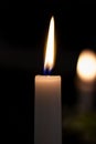 A close up shot of a lit thin white candle burning in the darkness, with in the background a blurred one. The flame is blue at the Royalty Free Stock Photo