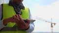 Close up shot of male engineer in uniform standing at construction site and tapping on tablet using gadget outdoor at