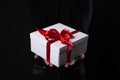 Close up shot of male hands holding a small gift wrapped with red ribbon. Small gift in the hands of a man on black background. Royalty Free Stock Photo