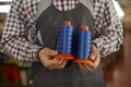 Close up of blue thread bobbins in hands of dressmaker, shoemaker or factory worker