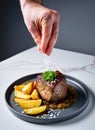 Close up shot of a man\'s hand pouring salt on a sirloin steak dish. AI generated