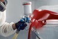 Close-up shot of man using a spray gun and painting red car wing in workshop. Royalty Free Stock Photo