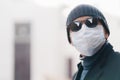 Close up shot of man wears hat and disposable medical mask, afraids of getting infected with coronavirus, poses against blurred