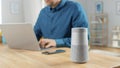 Close Up Shot of a Modern Silver Bluetooth Speaker Standing on a Table at Home. Man in the Backgro Royalty Free Stock Photo