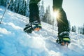 Close up shot of mountain boots with crampons and snow gaiters with backlight sun beams and snowy spruces on background . High
