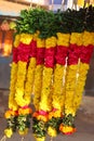 Close up shot of multicolored marigold flowers, rose flowers, jasmine flowers and green betel leaf garland hanging on rod in