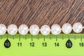 Close-up shot of a necklace made of pearl beads and a ruler on a wooden background.