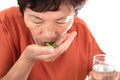 Close-up shot of old Chinese lady putting medicine into mouth in front of white background