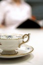 Close up shot of an old fashioned china tea cup and saucer, with an out of focus person in the background, reading a book Royalty Free Stock Photo