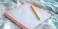 A close up shot of a pink notebook with a yellow pencil on a bed with white and blue sheets Royalty Free Stock Photo