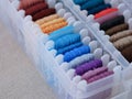A close-up shot of a plastic sorting box full of bobbins with different colour embroidery threads on a beige canvas background Royalty Free Stock Photo