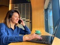 Close-up shot of pretty lady typing on laptop and speaking on smartphone while sitting in cafeteria. Freelance work Royalty Free Stock Photo