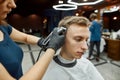 Close up shot of a professional barber girl working with hair clipper, making modern haircut for a young guy visiting Royalty Free Stock Photo