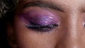 Close up shot on purple glowing wet makup eye of beautiful African fashion model