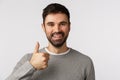Close-up shot reliable and pleased smiling, happy man with beard in grey sweater, show thumb-up give approval, like or