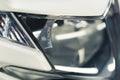 Close-up shot of shiny front light headlight of white modern car. Car detailing concept. Horizontal indoor shot.