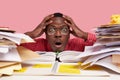 Close up shot of shocked stupefied black African American man keeps both hands on head, looks through pile of books and