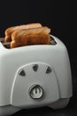 Close-up shot of slightly burnt white bread toasts sticking out of a toaster on the black background. Ready toasts with a dark Royalty Free Stock Photo