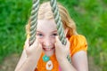 Close up shot of smiley pretty blonde girl`s face while clinging to a rope. Focus on eyes, blurry background