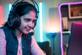 close up shot of Smiling girl playing live video game on laptop by talking on headphones at home on neon background - Royalty Free Stock Photo