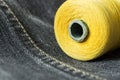 Close-up shot of a spool of yellow thread on dark grey denim.