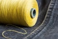 Close-up shot of a spool of yellow thread on dark grey denim.