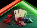 Two aces standing leaning on chips piles, some of them laying nearby on green cover of playing table, under green and