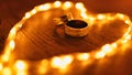 Close-up shot of two golden engagement rings in the middle of glowing heart shaped lights on a table Royalty Free Stock Photo