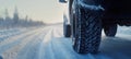 Close-up shot of vehicle tire on snowy surface with visible brake trace. Snowy highway stretches into background enhancing winter