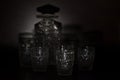 Close up shot of whiskey crystal decanter and glasses in the dark with a background of shadows