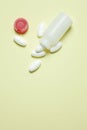 Close-up shot of a white medicine container and assorted pill capsules on a yellow tabletop