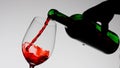 Close up shot of wine glass isolated on white background in studio. Female holding bottle and spilling red wine into a Royalty Free Stock Photo