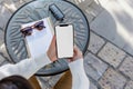 A close up shot of a woman's hand holding an phone with a blank screen sitting at an outdoor cafe table, notebook on Royalty Free Stock Photo