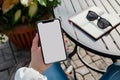 A close up shot of a woman& x27;s hand holding an phone with a blank screen sitting at an outdoor cafe table, notebook on Royalty Free Stock Photo